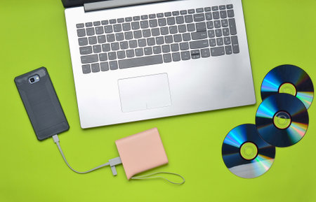 Laptop, smartphone, power bank, CD drives, on a green background. Digital media, gadgets.