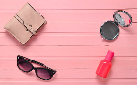 Women's accessories on a pink wooden background. Mirror, sunglasses, purse, perfume bottle. Top view.の写真素材