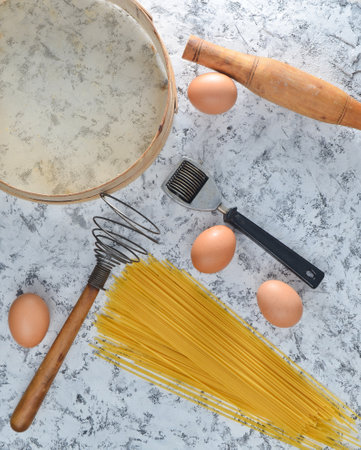 Space for cooking. Kitchen tools and ingredients for cooking on a white concrete table. Pasta, sieve, whisk, rolling pin, eggs. Top view.の写真素材