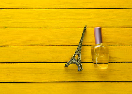 A perfume bottle and a souvenir statuette of the Eiffel Tower on a yellow wooden background.の写真素材