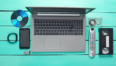 Modern and obsolete devices and gadgets on a turquoise wooden table. Laptop, audio and video...