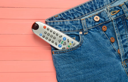 Tv remote in a jeans pocket on a pink wooden background.の写真素材