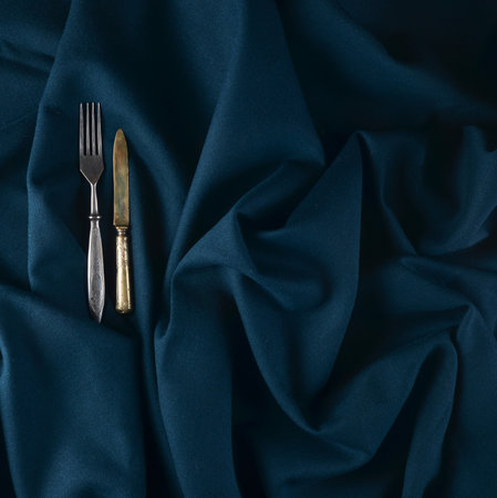An antique knife and fork on a dark cloth tablecloth.の写真素材