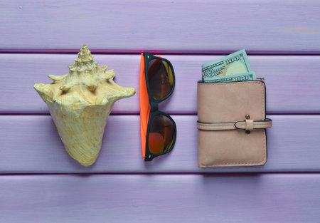The concept of a summer beach resort. Wallet, shell, hipster sunglasses on a violet wooden...