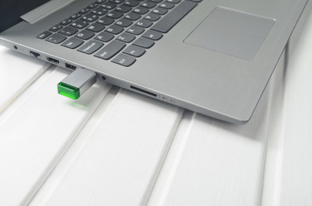 Usb flash drive inserted into the laptop socket on a white wooden desk. Modern technologies.