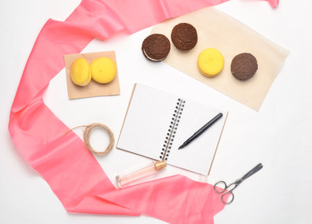 Flat lay of cookies, macaroon notebook, pens, scissors, perfume bottle on white background. Top view.の写真素材
