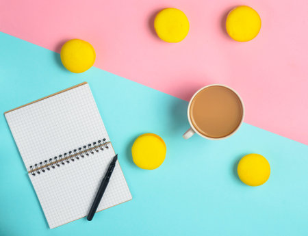 Notebook with a pen, a cup of coffee and yellow macaroons on a pastel colored background. Trend of minimalism. Top view. Flat lay.の写真素材