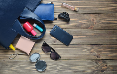 What's in the women's bag? Women's trendy accessories on a wooden background. Smartphone, perfume bottle, power bank, mirror, sunglasses, lipstick. Top view.の写真素材