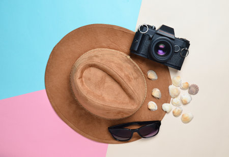 The concept of a resort on the beach. Felt hat, sunglasses, vintage film camera, seashells on a colored paper background.の写真素材