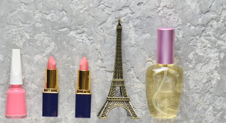 Women's cosmetics from Paris. Two pink lipsticks, a perfume bottle, nail polish, a statuette of the Eiffel tower on a gray concrete background. Top view.の写真素材