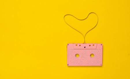 Heart shape from audio cassette tape over yellow paper background, top view. Hipster Love.の写真素材