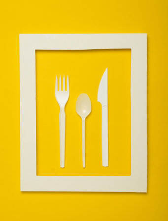 Plastic cutlery for picnics in a white frame on a yellow background. A disposable spoon, fork, knife. Top view, minimalistic trend.の写真素材