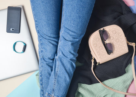 A girl in jeans sits on the floor among gadgets and accessories. Top view.