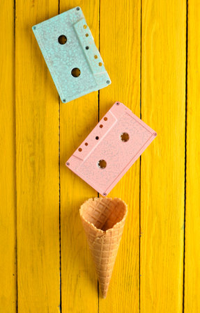 Colored pastel audio cassette and empty waffle horn on a yellow wooden background. Top view,...