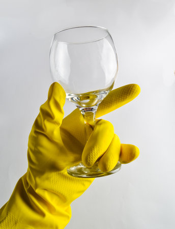 A man's hand in a yellow latex glove holds a clean glass wine glassの写真素材