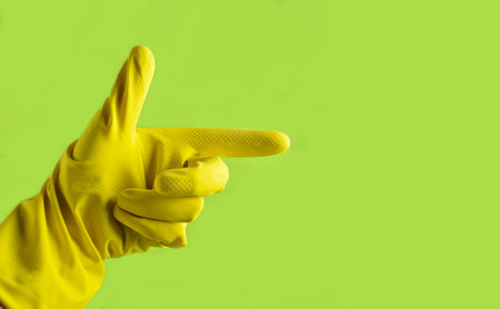 Hand with yellow rubber glove is pointing in the side on a green background, cleaning concept, copy spaceの写真素材