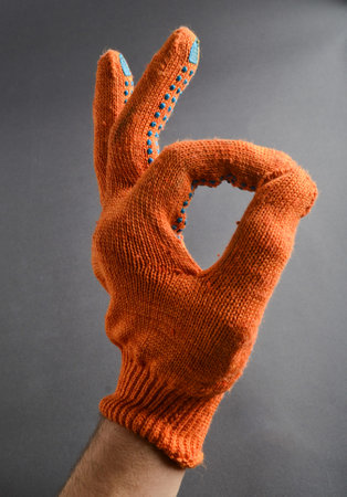 Hand with orange working gloves shows thumbs symbol okay on gray background.