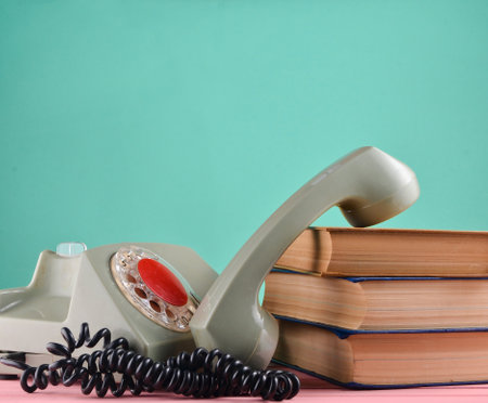 Retro rotary telephone, stack of books on a desk isolated against a blue pastel wallの写真素材