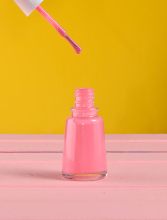 Open bottle of pink nail polish on a yellow backgroundの写真素材
