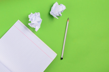 Top view of notebook with pencil and white crumpled paper ball on green background. Concept of no...
