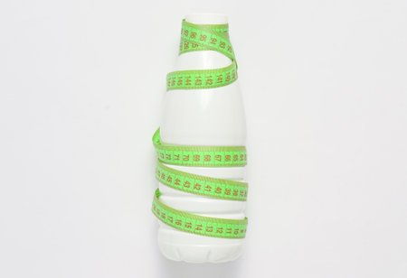 Bottle of yogurt wrapped in a ruler on a  white background, dietary, slimming concept, top view