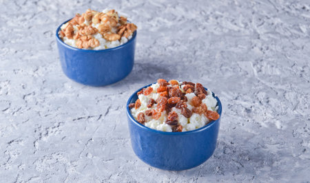 Ceramic bowls of cottage cheese with raisins and walnuts on a gray concrete table.