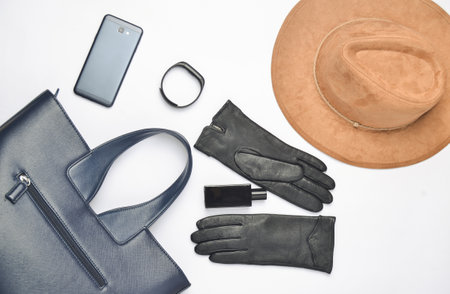 Female accessories and gadgets on a white background. Bag, hat, gloves, smartphone, smart watch, perfume bottle. Autumn spring collection. Top view. Flat lay.の写真素材