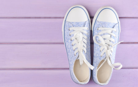 Female hipster sneakers with white laces on a pastel violet wooden floor, top viewの写真素材