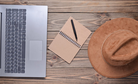 Laptop, felt hat, notebook and pen on a wooden table. Journalism concept, top view, flat layの写真素材