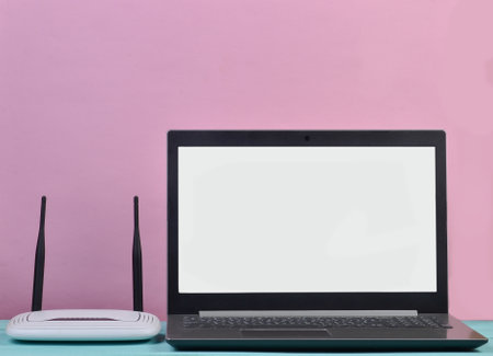 Wi-fi router, white laptop screen on a wooden table against a pastel pink wall. Copy space, minimalismの写真素材