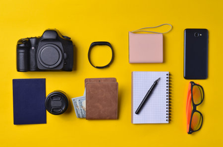 Gadgets and accessories layout on a yellow background. Power bank, photographic equipment, purse with dollars, smart clock, smartphone, notebook, sunglasses. The concept of travel, objects, top viewの写真素材