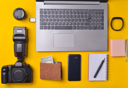 Equipment photographer,  laptop, purse with dollars,  smartphone, smart watch, power bank, on a yellow background. Freelance concept, gadgets for work, objects, top view, flat layの写真素材
