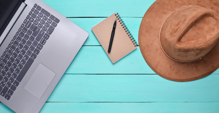 Laptop, felt hat, notebook and pen on a blue wooden table. Journalism concept, top view, flat layの写真素材