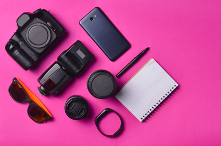 Gadgets and accessories layout on a pink background. Photographic equipment, purse with dollars,...