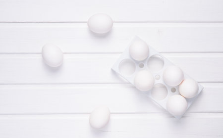Plastic tray with white eggs on a white  wooden table, minimalism trend, top viewの写真素材