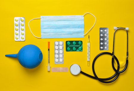 Medical equipment on a yellow background. Enema, blisters pills, notebook, stethoscope, syringe, thermometer. Medical concept, top view, flat lay styleの写真素材