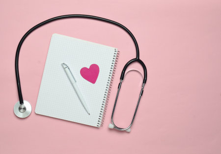 Notepad with pen, decorative heart, stethoscope on pink pastel background, medical concept, top view, minimalism trendの写真素材