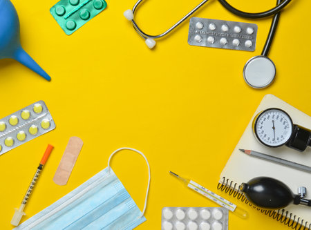Medical equipment on a yellow background. Enema, blisters pills, notepad, stethoscope, syringe, thermometer, manometer. Medical concept, top view, flat lay style, copy spaceの写真素材