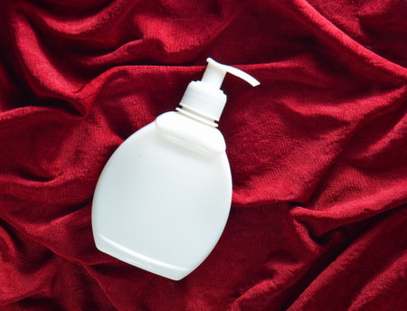 White plastic bottle of cream on a red silk backgroundの写真素材