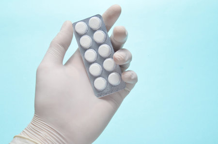 Medic's hand with white latex gloves holds a blister of pills on a blue background. Medical concept