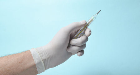 Medical man's hand with white latex gloves holds the thermometer on a blue background. Medical conceptの写真素材