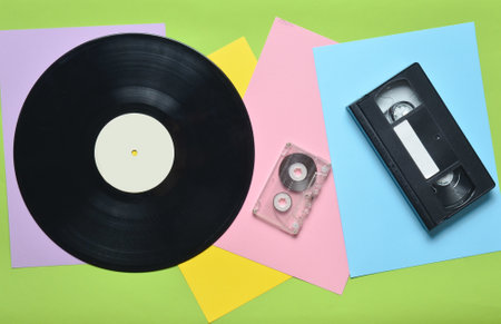 Vinyl record, audio cassette, video cassette on a multi-colored paper background. Retro style. top viewの写真素材