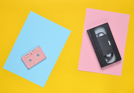 Audio cassette and video cassette on a colored paper background. Retro entertainment technology from...