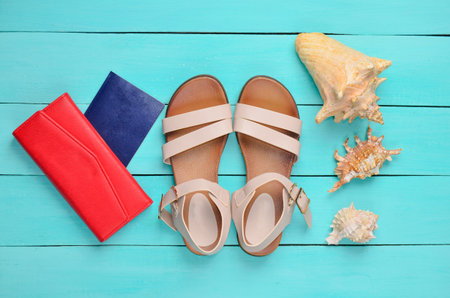 Fashionable women's sandals, passport, red purse, seashells on a blue wooden floor. The concept of traveling to the sea. Top view.の写真素材