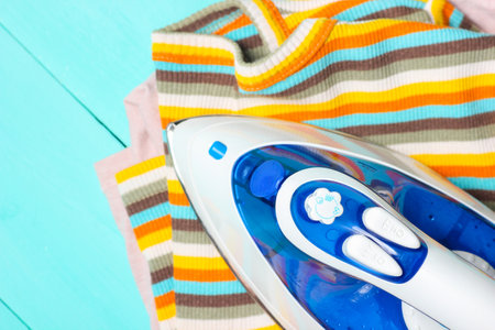 The iron strokes a yellow striped T-shirt on wooden blue table. Top viewの写真素材