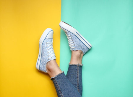 Women's legs in tight, torn jeans, sneakers on yellow blue pastel background. Top view, minimalism, copy spaceの写真素材
