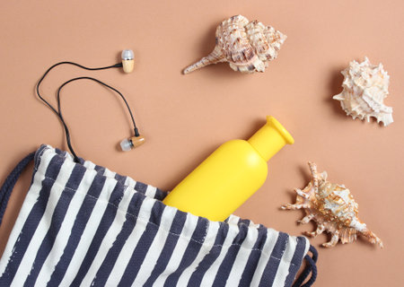 Beach bag, seashells, earphones, bottle of suntan cream on a brown background, beach season, rest on the sea. Top view, minimalismの写真素材