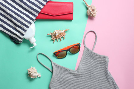 Beach accessories on a colored pastel background. Beach bag, T-shirt, sunglasses, purse, sunblock, cockleshells. Top Viewの写真素材