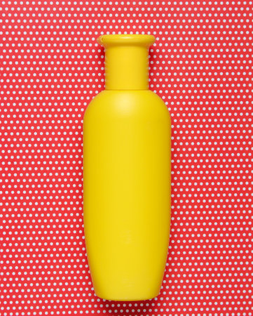 Yellow bottle of shampoo on creative red background in polka dot, top view