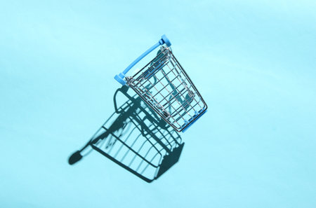 Mini shopping trolley for shopping on blue background, consumer concept, minimalism, top view, hard light, shadowの写真素材